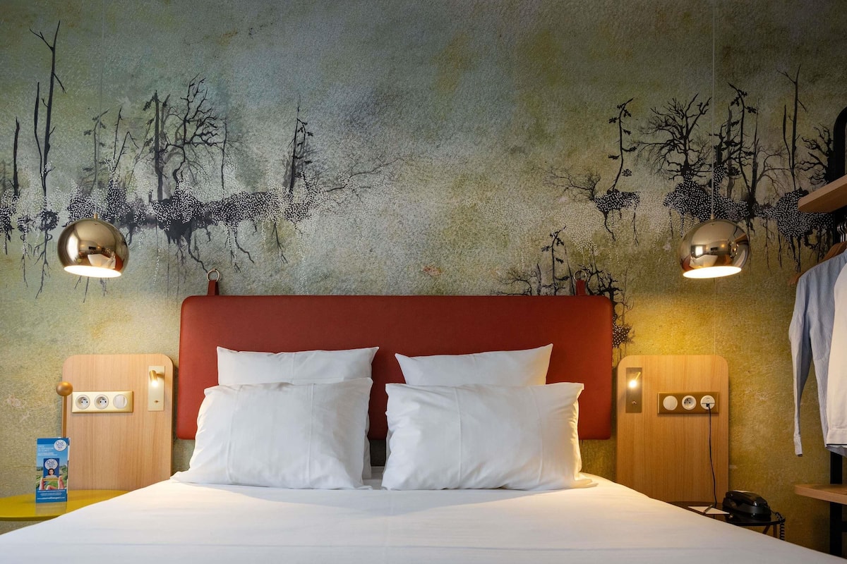 A hotel room with a large bed, two bedside tables, a red headboard, and a wall mural.