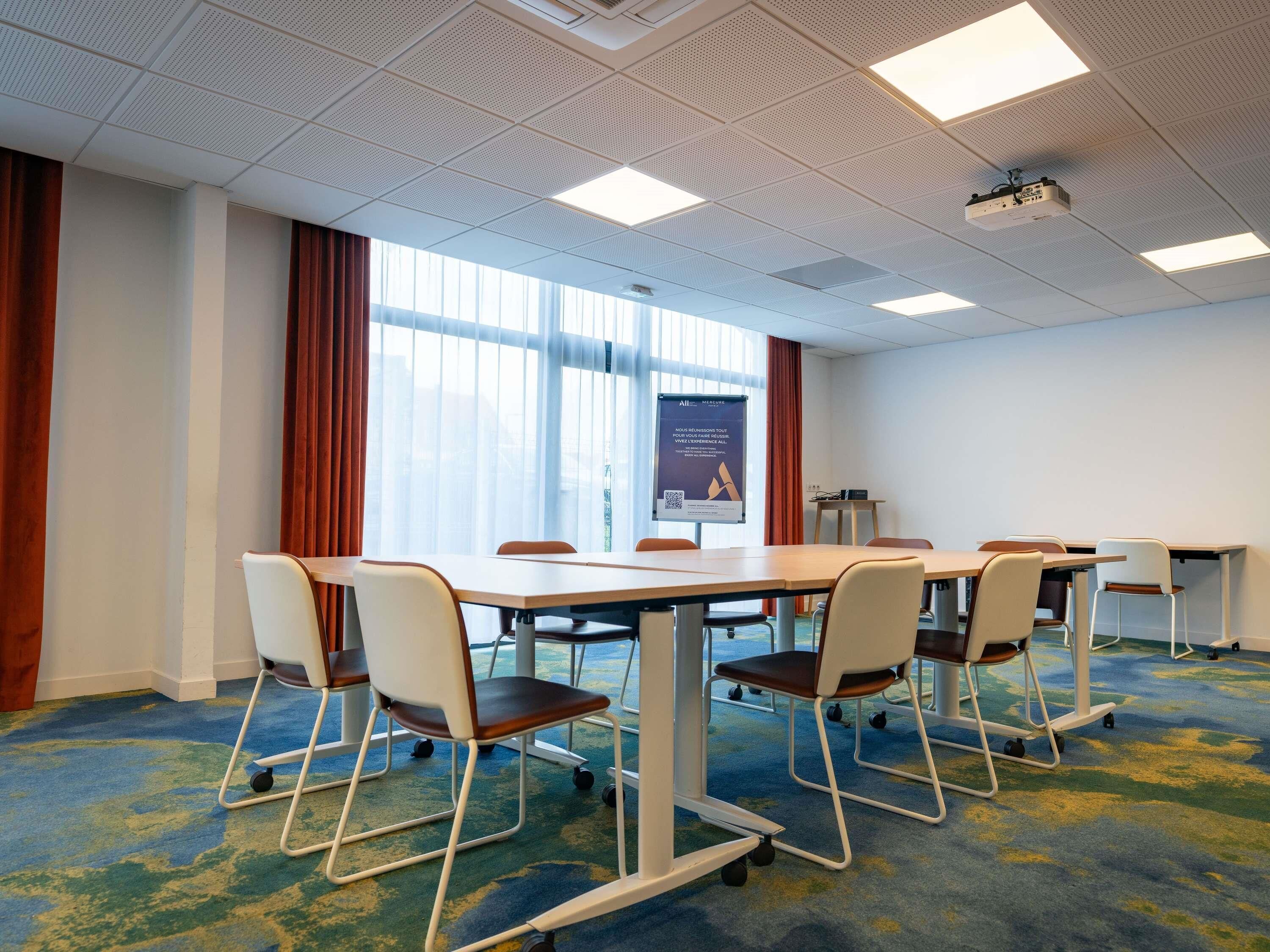 A conference room with a large table, chairs, a projector, and a presentation screen.