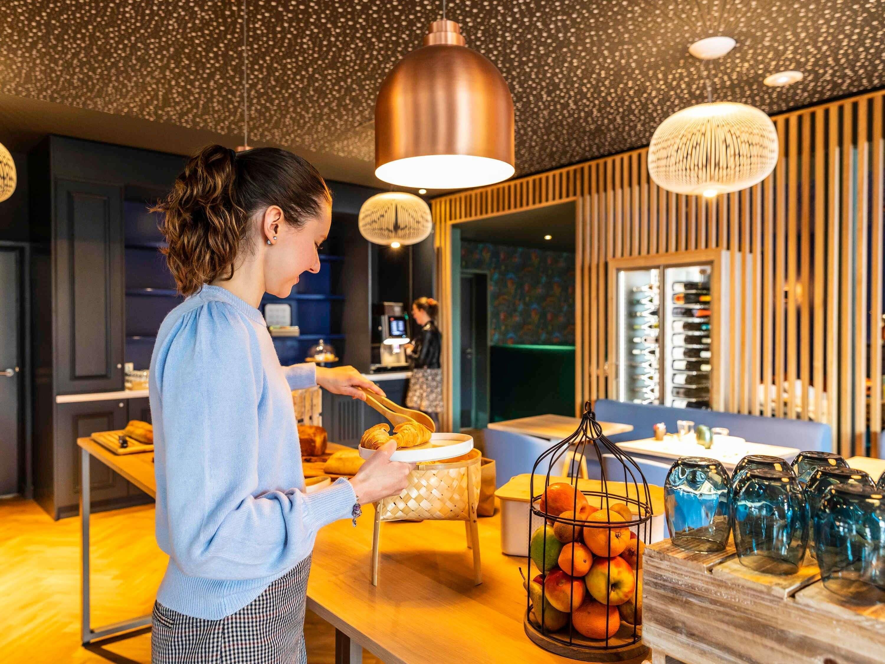 Une personne servant des plats dans un restaurant moderne, dont le décor est agrémenté d’éléments en bois et d’éclairages suspendus.