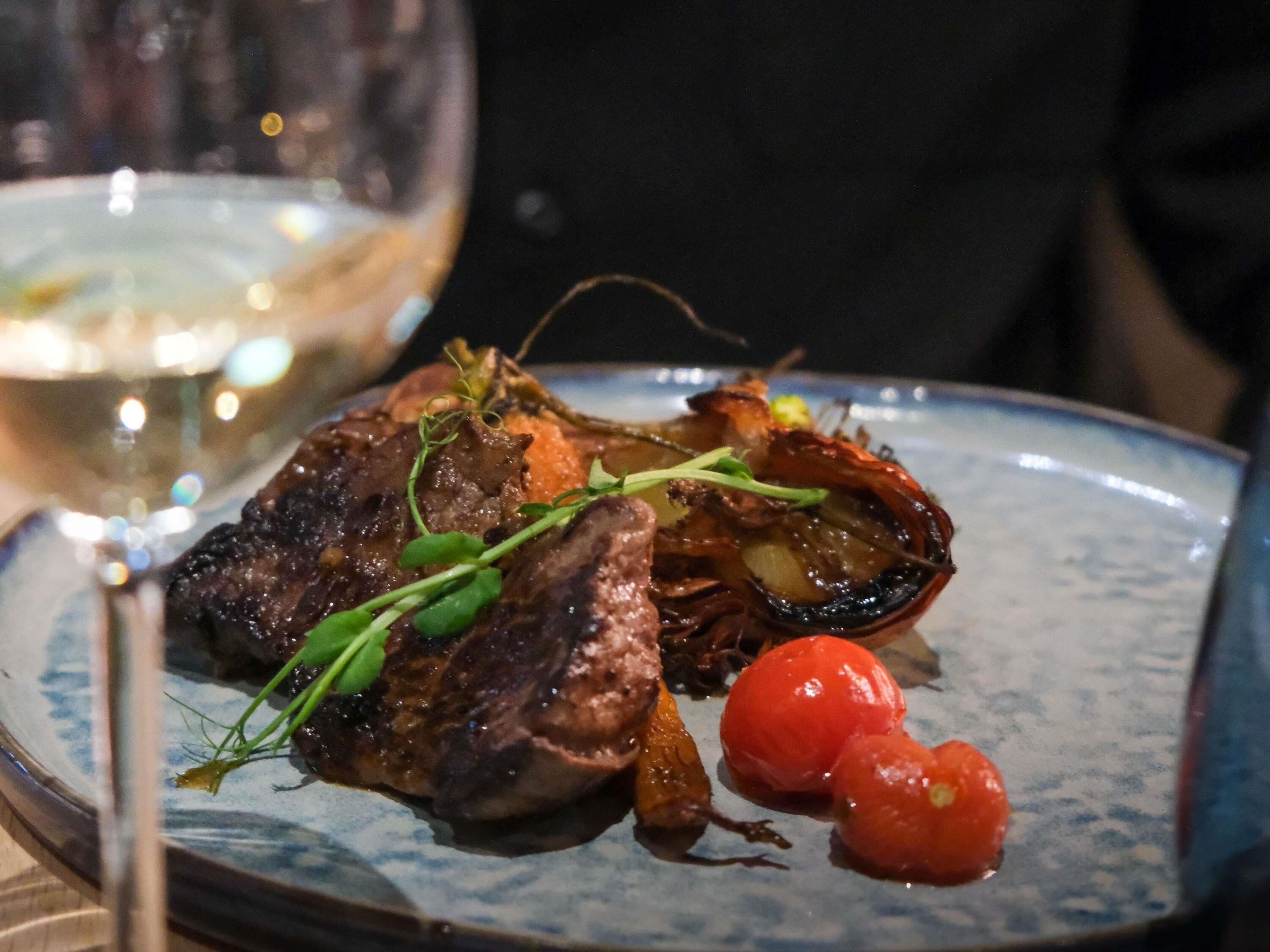 A plate with a dish of meat, possibly lamb, garnished with greens and accompanied by two cherry tomatoes.