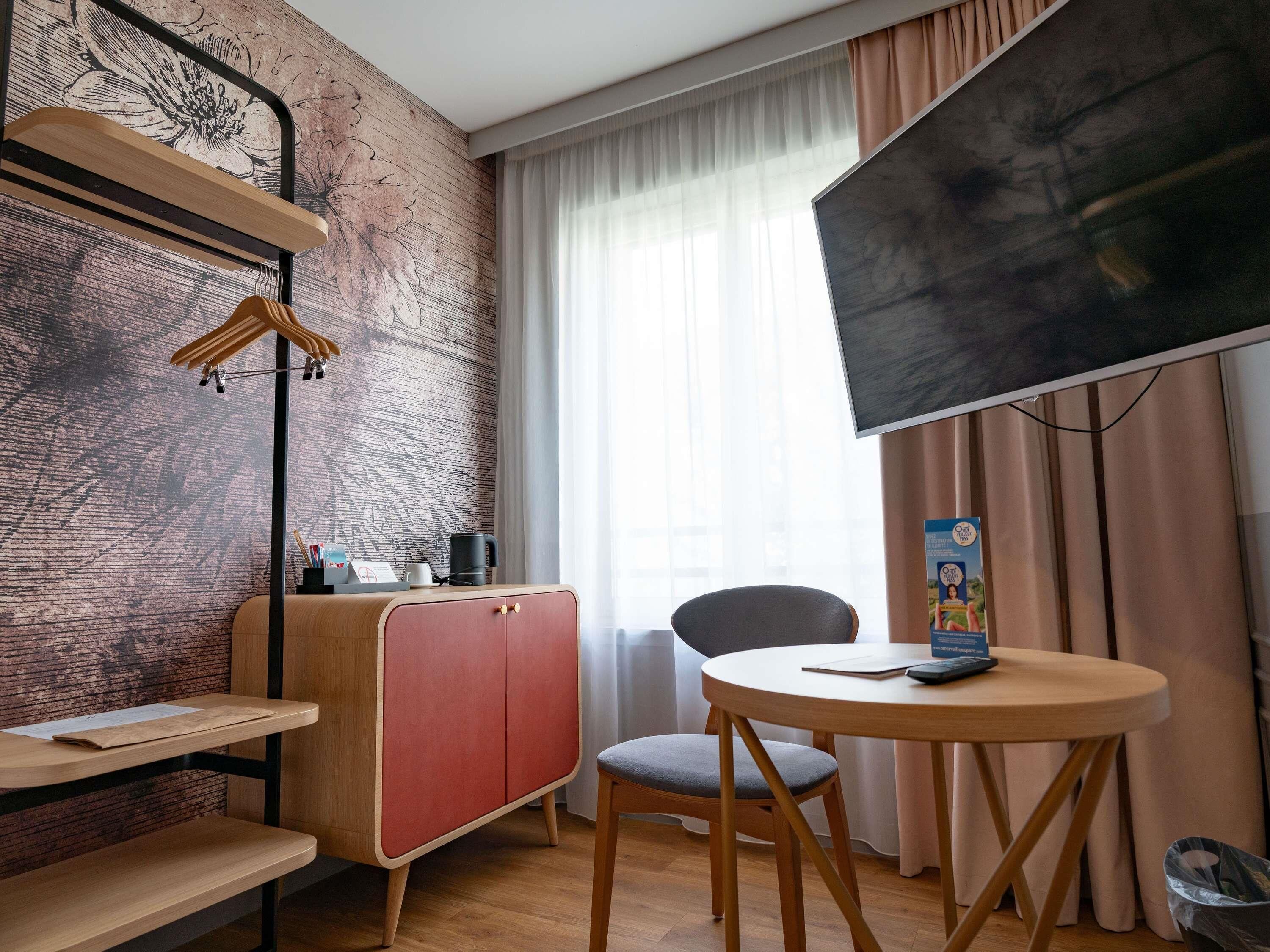 Een moderne kamer met een houten bureau, een rode kast, een grijze stoel, een televisie en een raam met gordijnen.