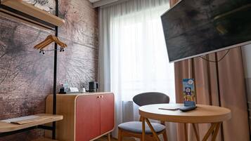 Een moderne kamer met een houten bureau, een rode kast, een grijze stoel, een televisie en een raam met gordijnen.