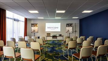 Una sala conferenze con file di sedie, uno schermo per proiettore e una presentazione sugli hotel Mercure.