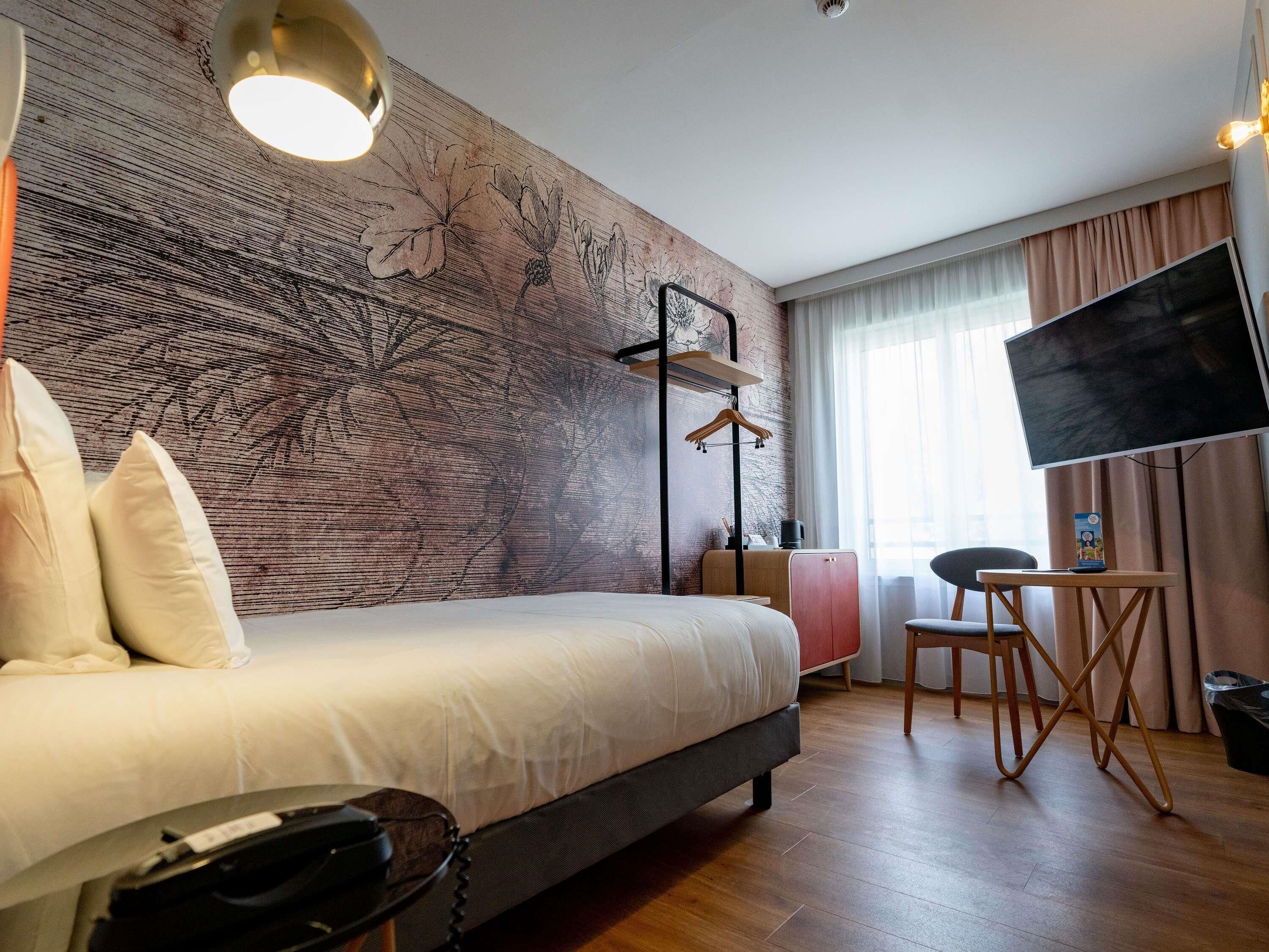 Una habitación de hotel con una cama grande, un escritorio con una silla, un televisor y un armario.