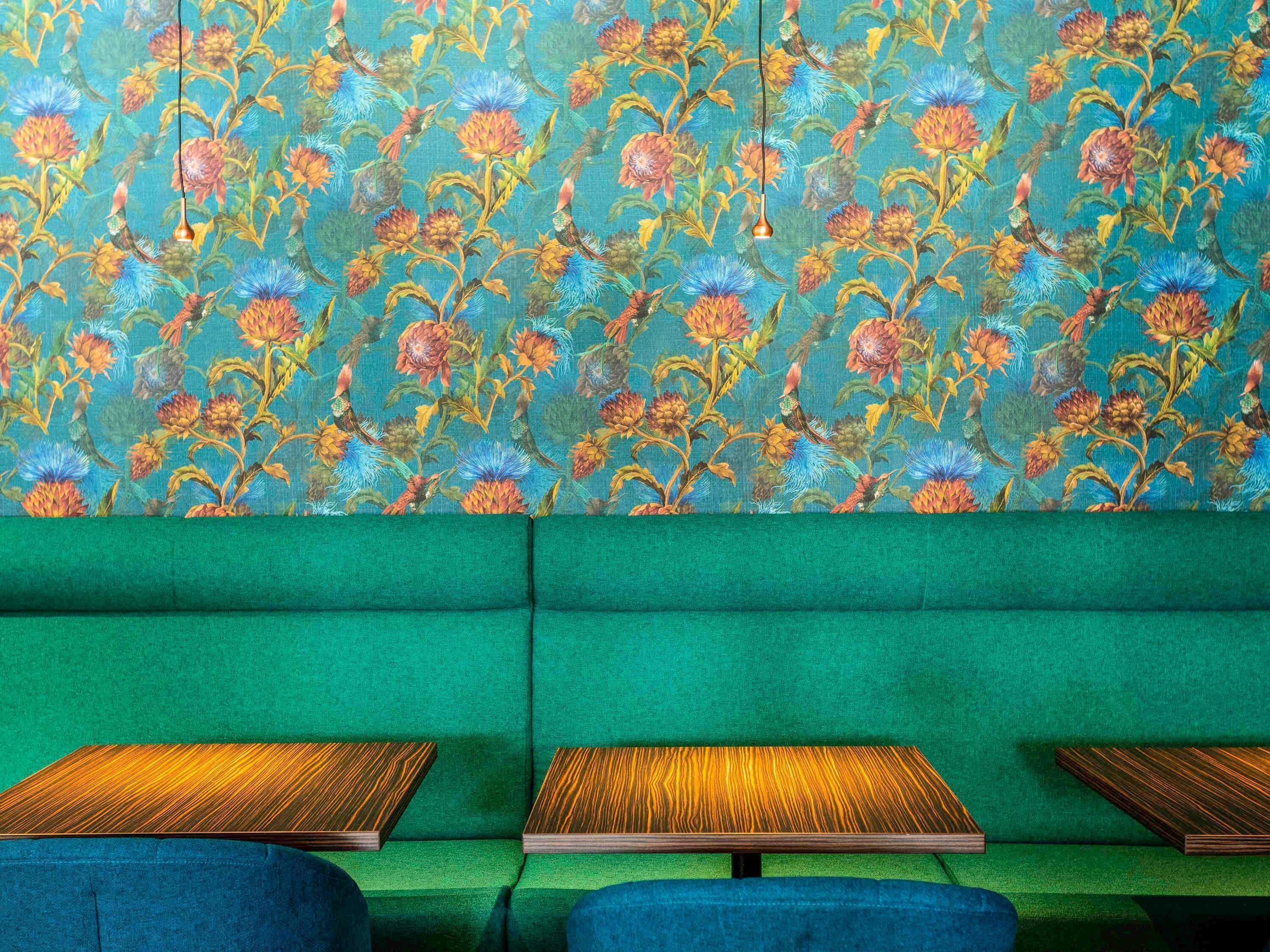 A green sofa with a floral patterned wall behind it and three wooden tables in front.