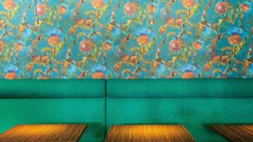 A green sofa with a floral patterned wall behind it and three wooden tables in front.