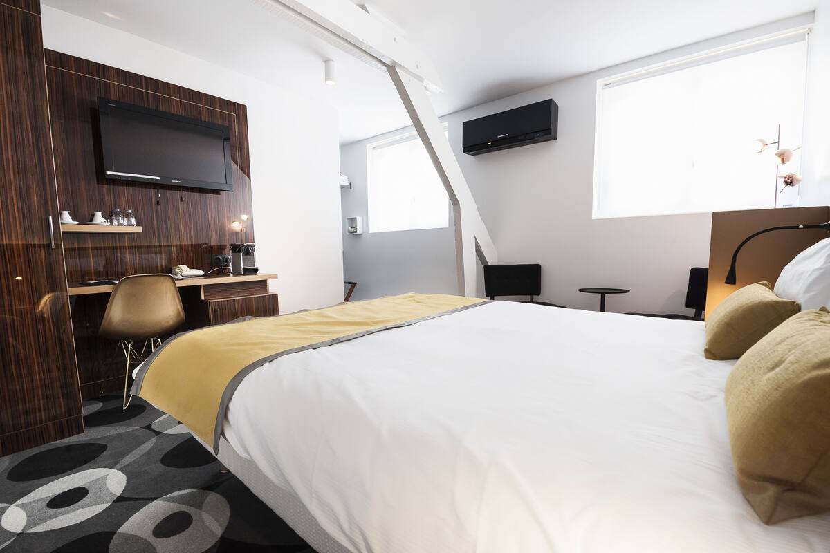 Ein modernes Hotelzimmer mit einem großen Bett, einem Schreibtisch mit Stuhl, einem wandmontierten Flachbildfernseher und einem Fenster mit Tageslicht.
