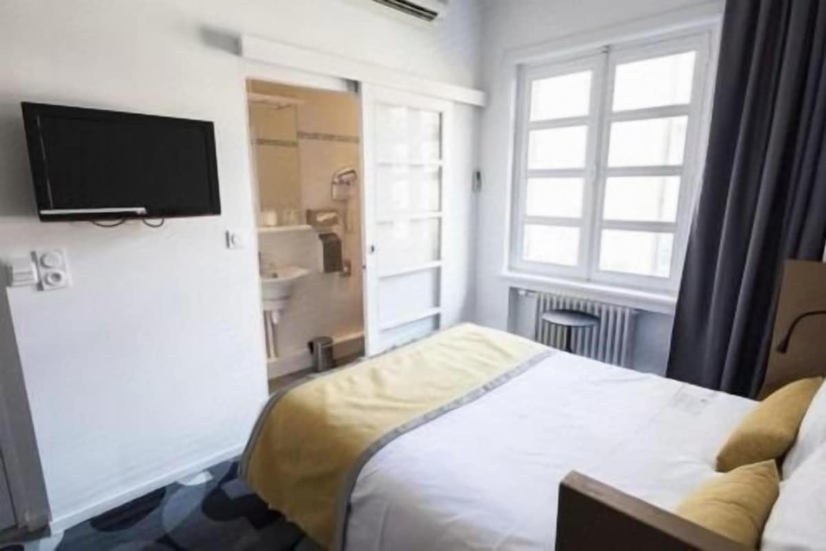 Een hotelkamer met een bed, een aan de muur bevestigde televisie en een raam met gordijnen.
