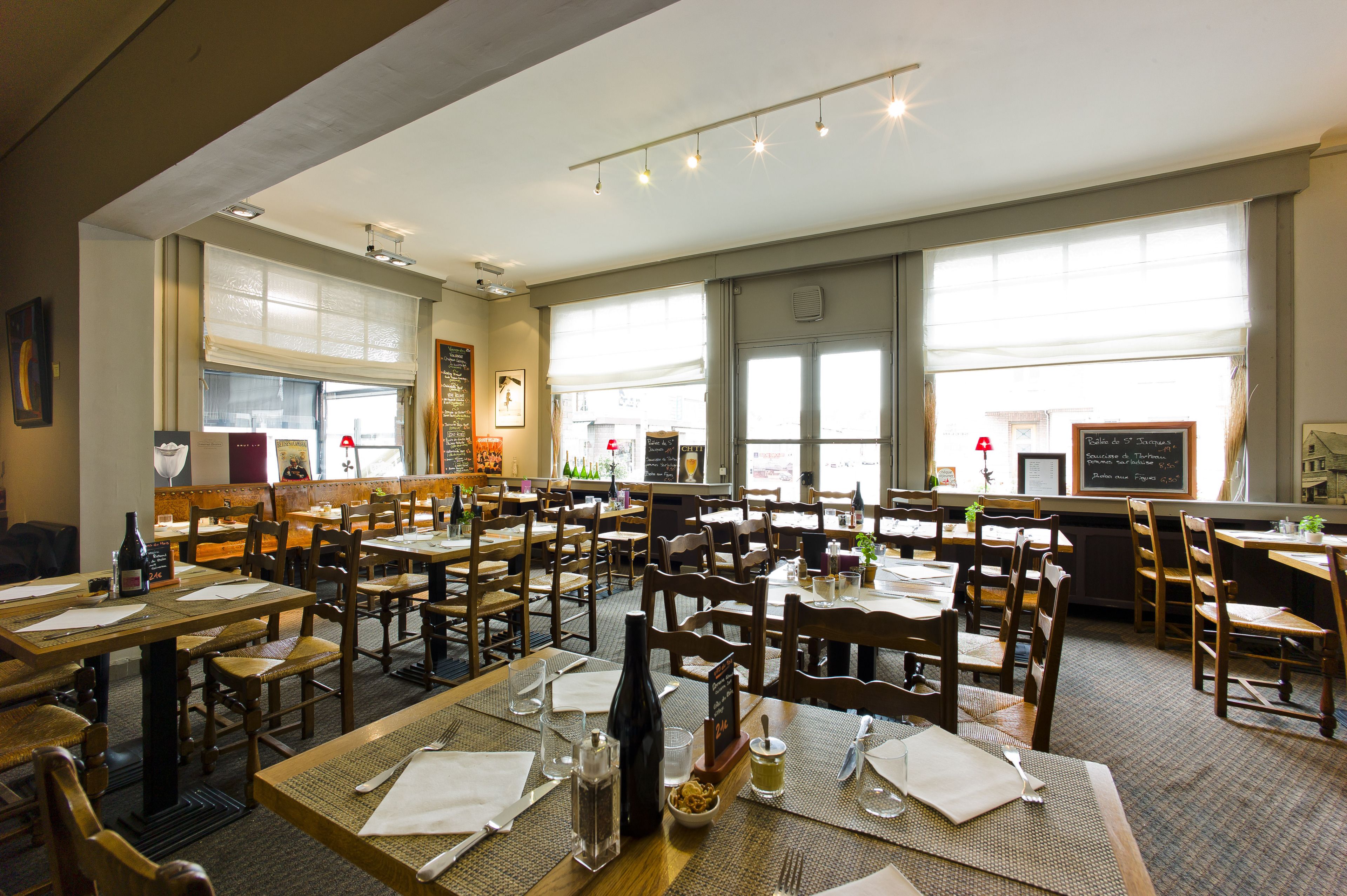 Un restaurante con varias mesas y sillas de madera, amplias ventanas y un menú en una pizarra.