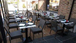 An outdoor seating area with tables and chairs, a brick wall, and a view of the street. - The Originals Boutique, Hôtel Auberge du Forgeron, Lille Sud (Seclin)