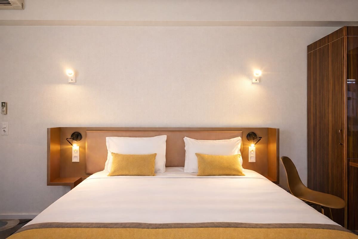 Ein Hotelzimmer mit einem großen Bett, zwei Nachttischen mit Lampen, einem Holzschrank und einem Sessel.