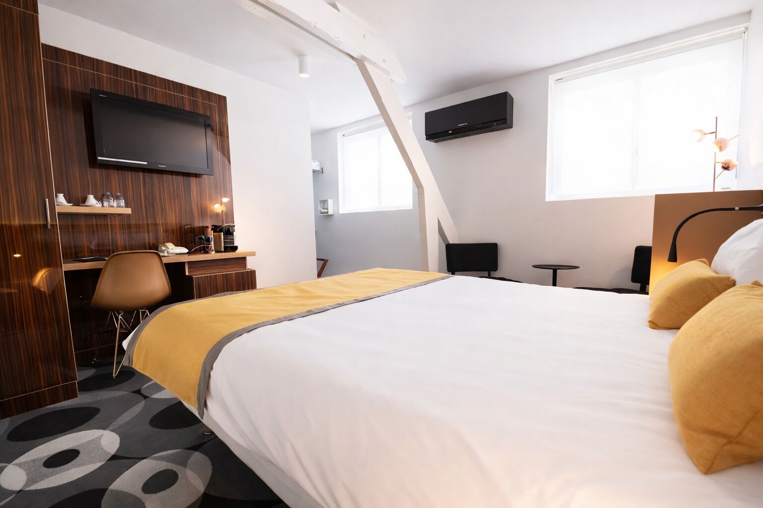 A modern hotel room with a large bed, a desk, a chair, a TV, and a window.