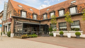 A hotel with a brick facade, large windows, and a covered outdoor seating area. - The Originals Boutique, Hôtel Auberge du Forgeron, Lille Sud (Seclin)