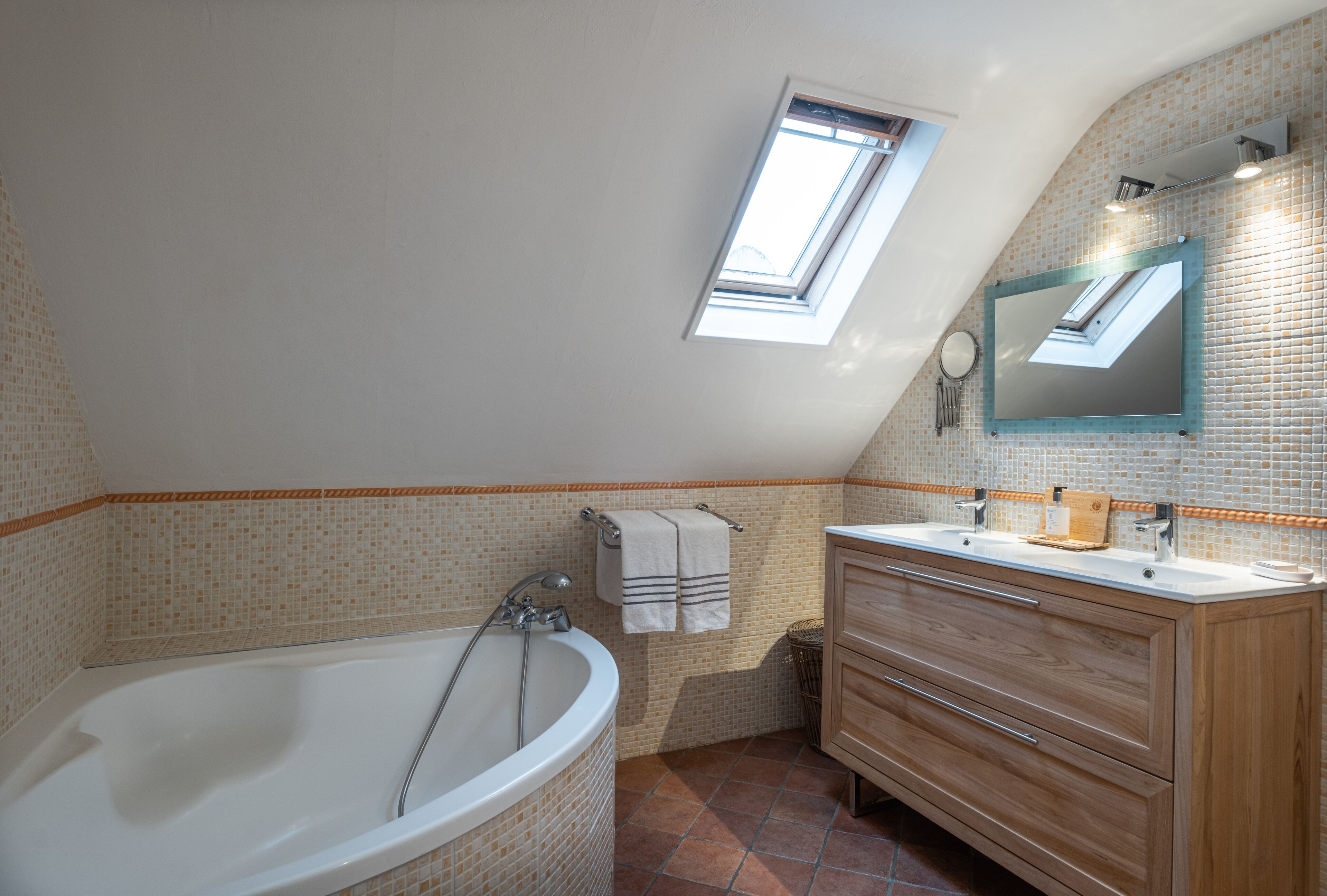 A bathroom with a freestanding bathtub, a wooden vanity, a mirror, and a skylight.