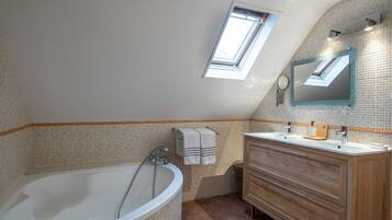 A bathroom with a freestanding bathtub, a wooden vanity, a mirror, and a skylight.