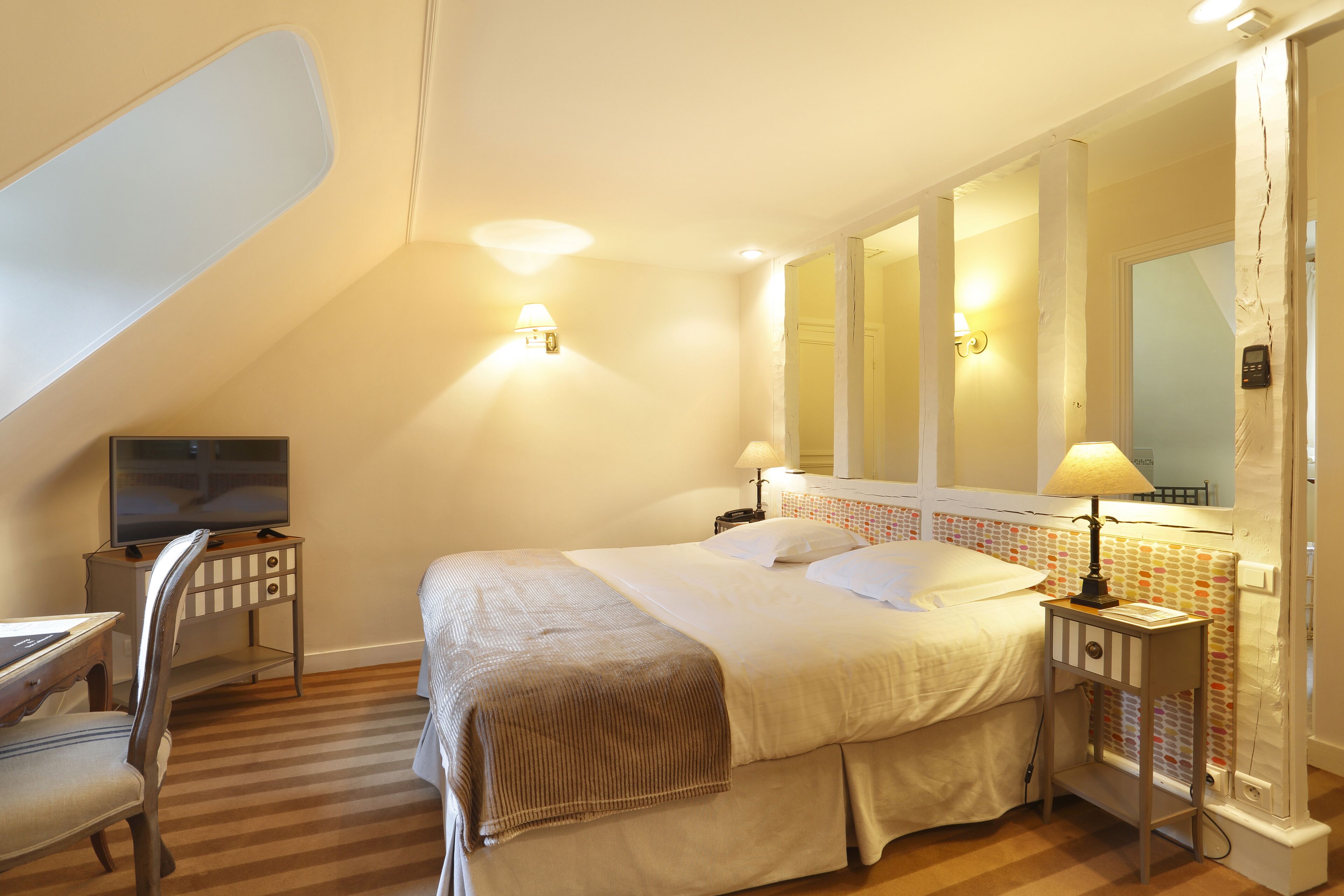Une chambre à coucher avec un lit, des tables de chevet, une télévision et un miroir.