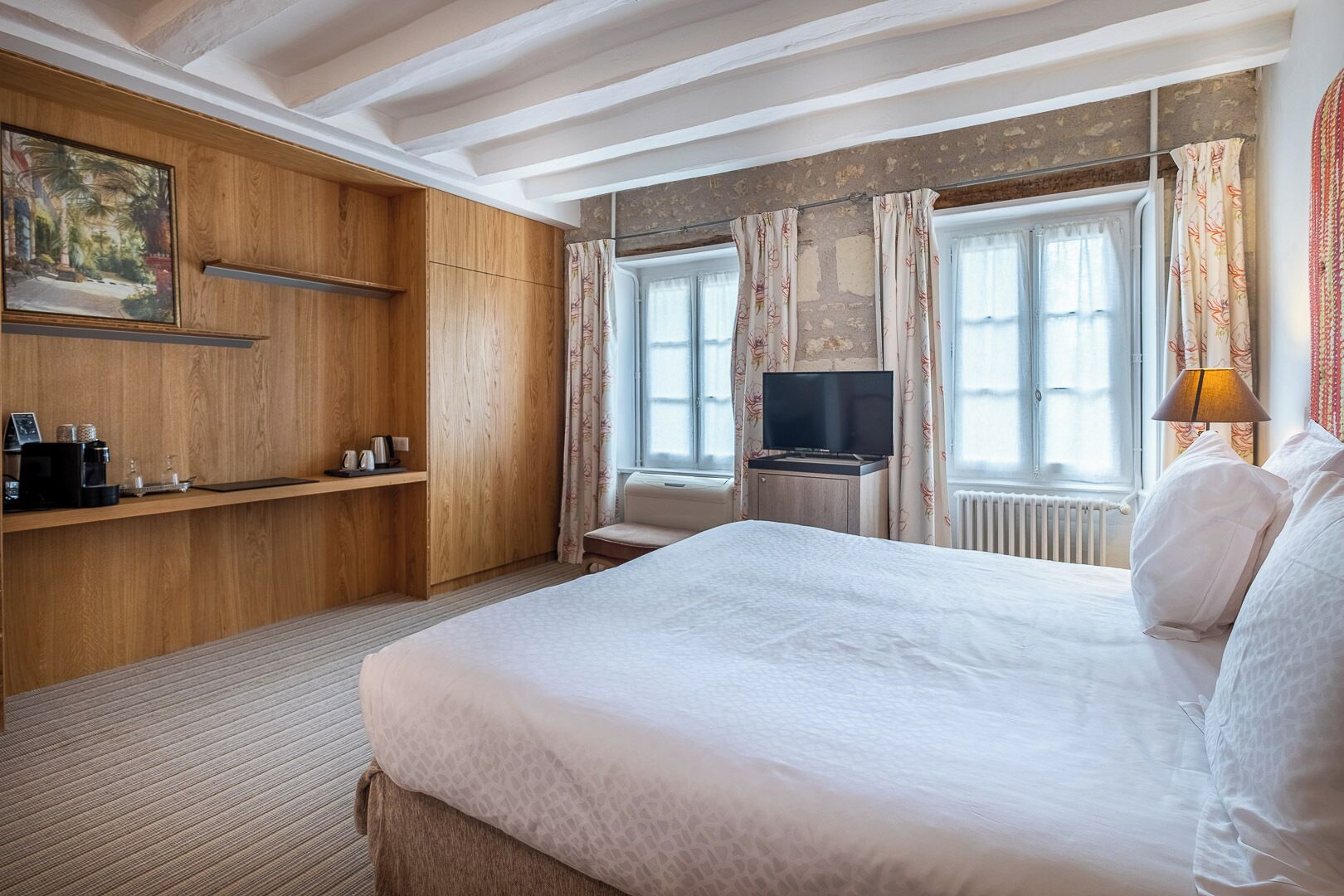 Habitación de hotel con una cama grande, armario de madera, televisor sobre una mesita y una ventana con cortinas.