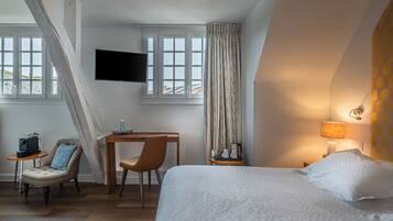 Habitación de hotel con cama, escritorio, silla, televisión y ventana con cortinas.