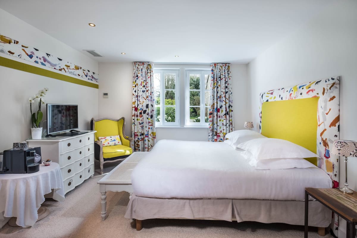 A bedroom with a bed, a desk, a chair, a television, and a window with curtains.