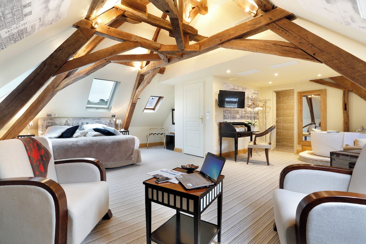 A spacious loft bedroom with a large bed, a desk with a laptop, and a seating area with chairs.