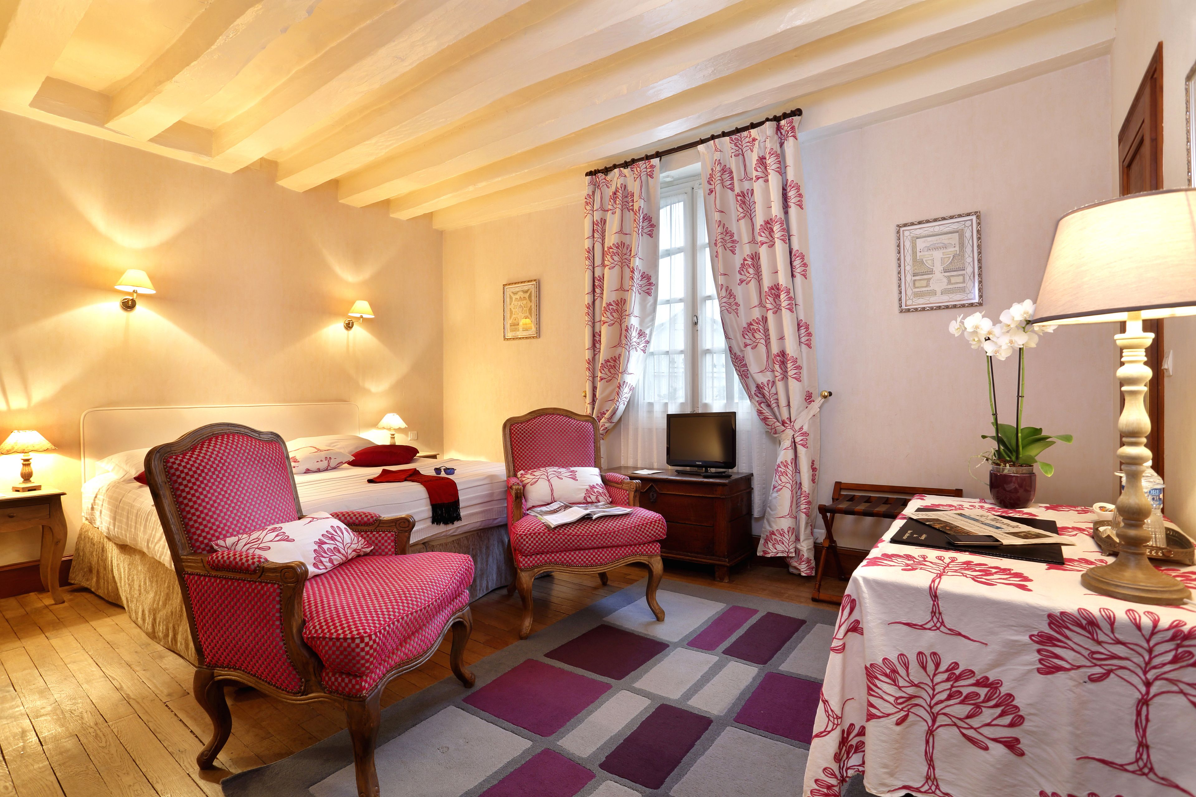 Une chambre avec deux lits simples, une télévision, un bureau avec une chaise et une table avec une lampe.