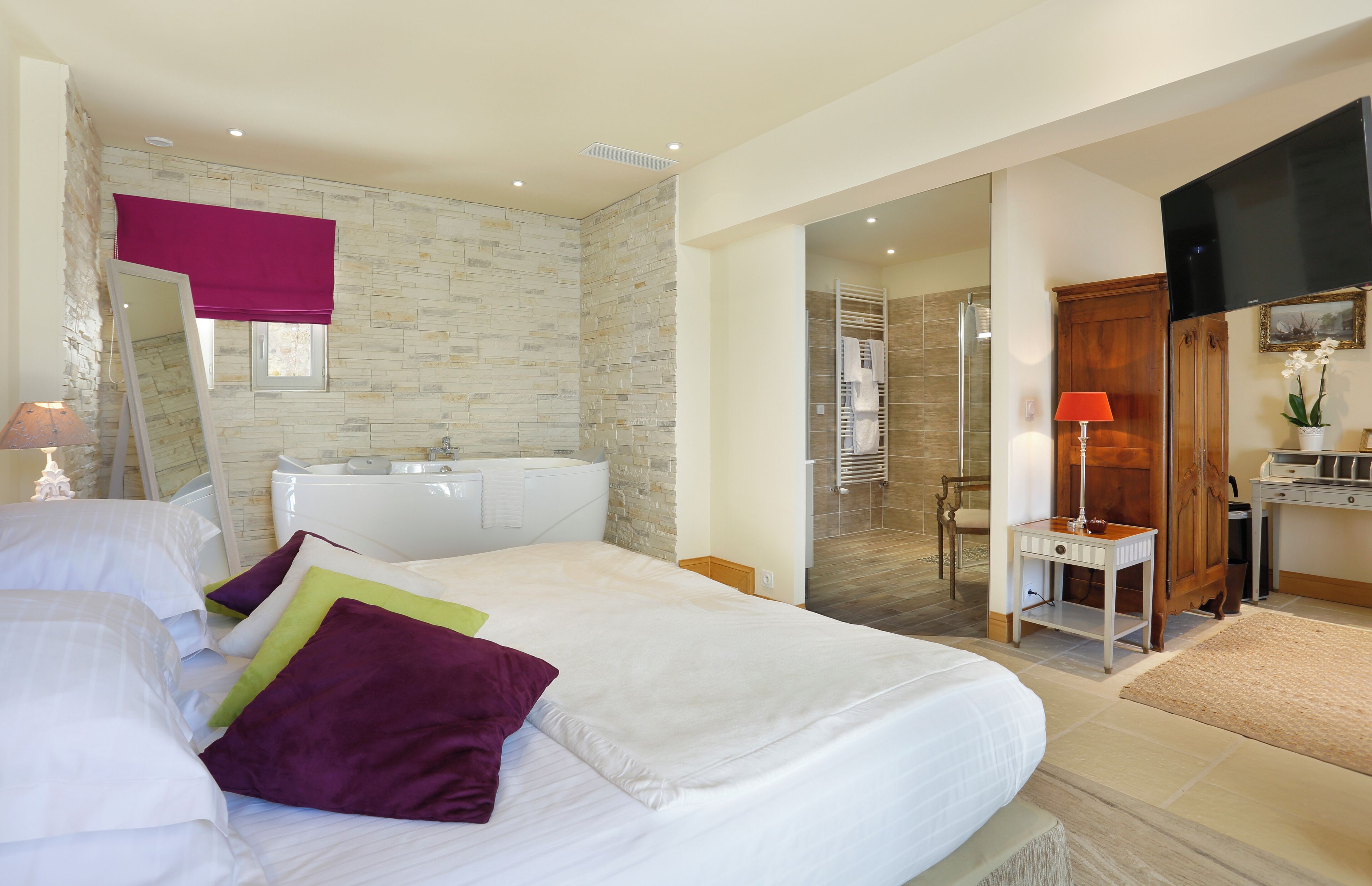 A bedroom with a large bed, a bathroom with a shower, and a TV in the corner.