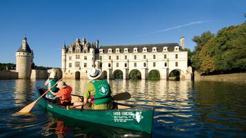 A green boat with two people paddling on a calm river, a historic building with arches and a tower in the background.