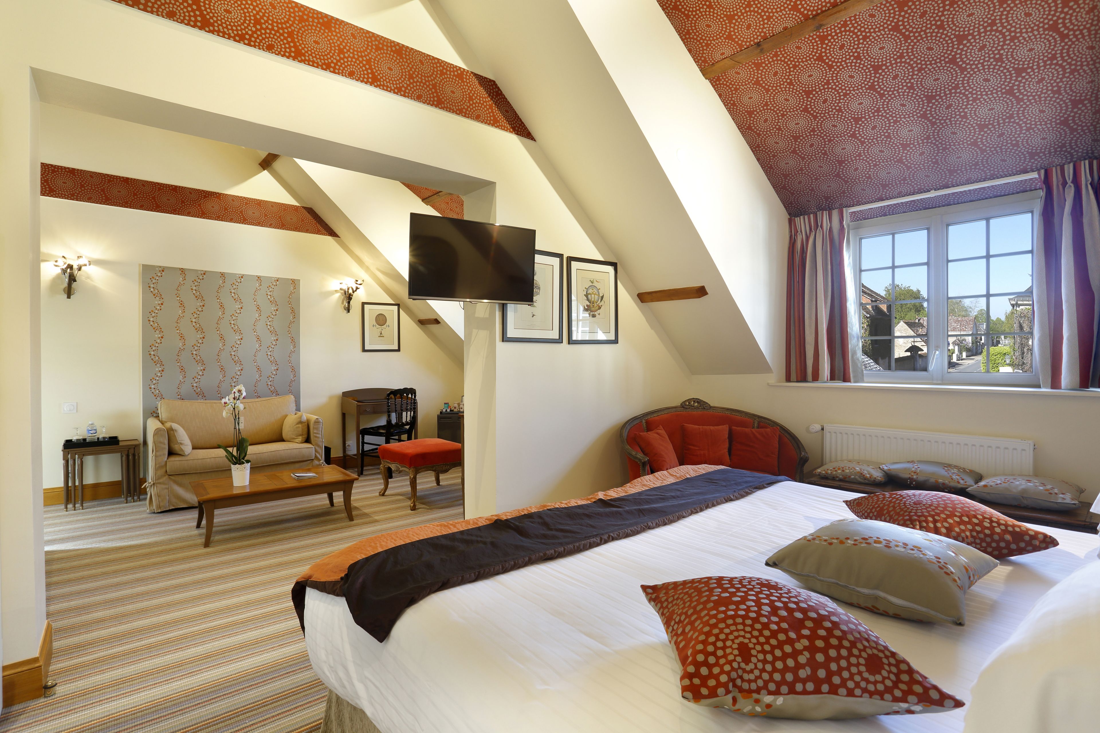 A spacious room with a large bed, a sofa, a television, and a window with curtains.