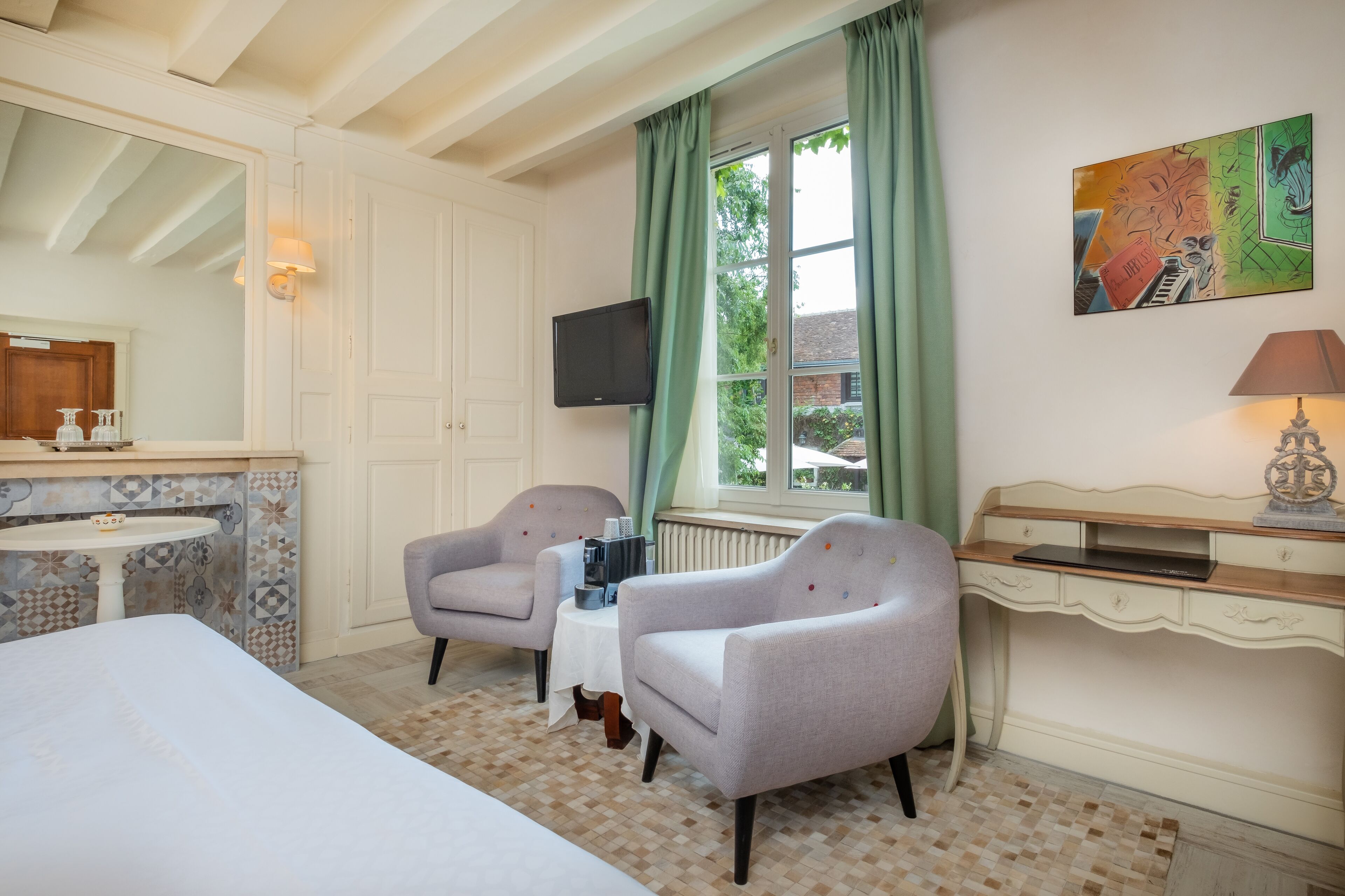 Habitación de hotel con una cama, dos sillones, una mesita, un escritorio con lámpara, un televisor y una ventana con cortinas.