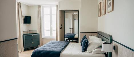 A hotel room with a bed, bedside table, lamp, and a television on the wall.