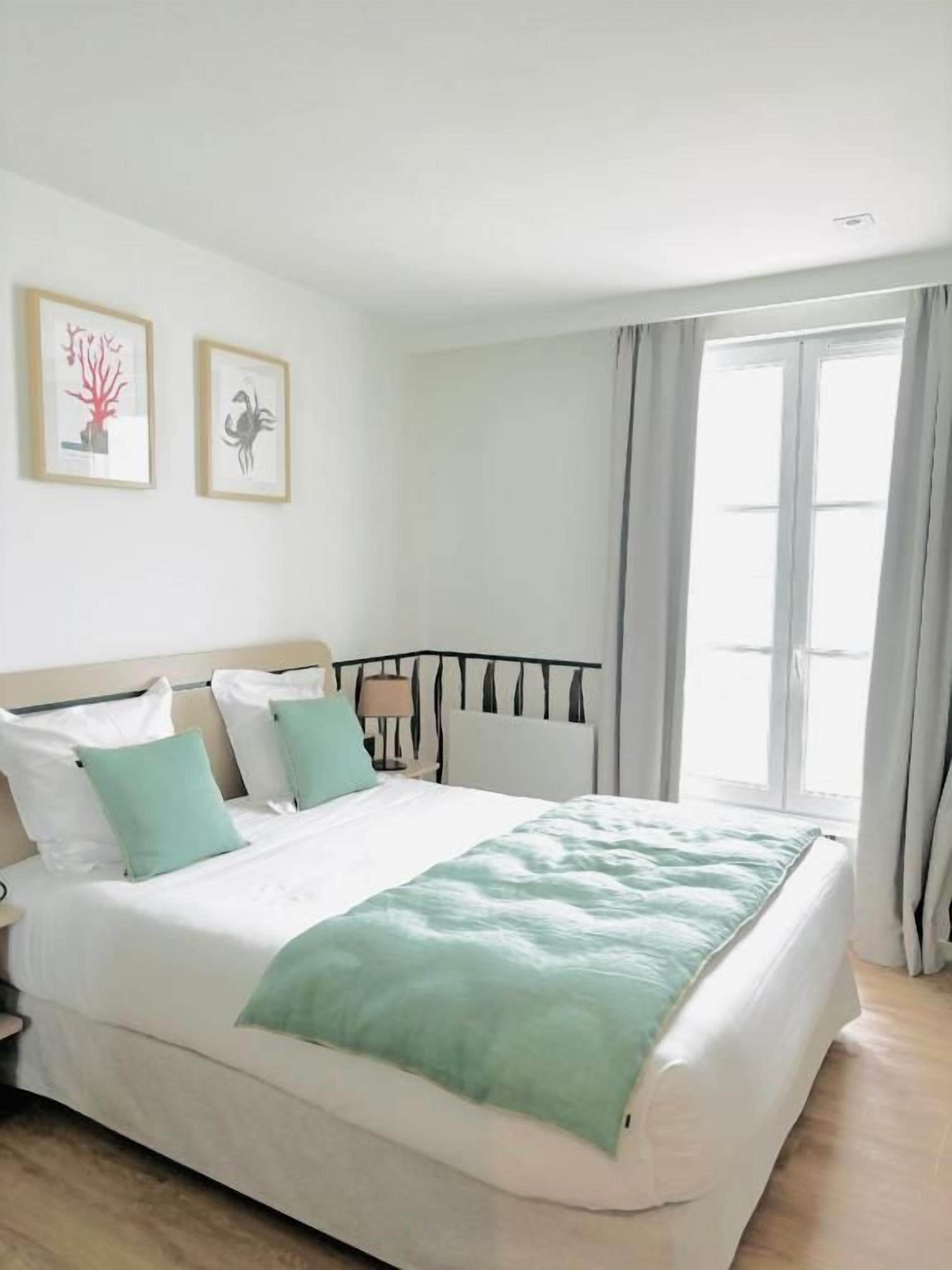Un dormitorio con cama, mesita de noche y ventana con cortinas.