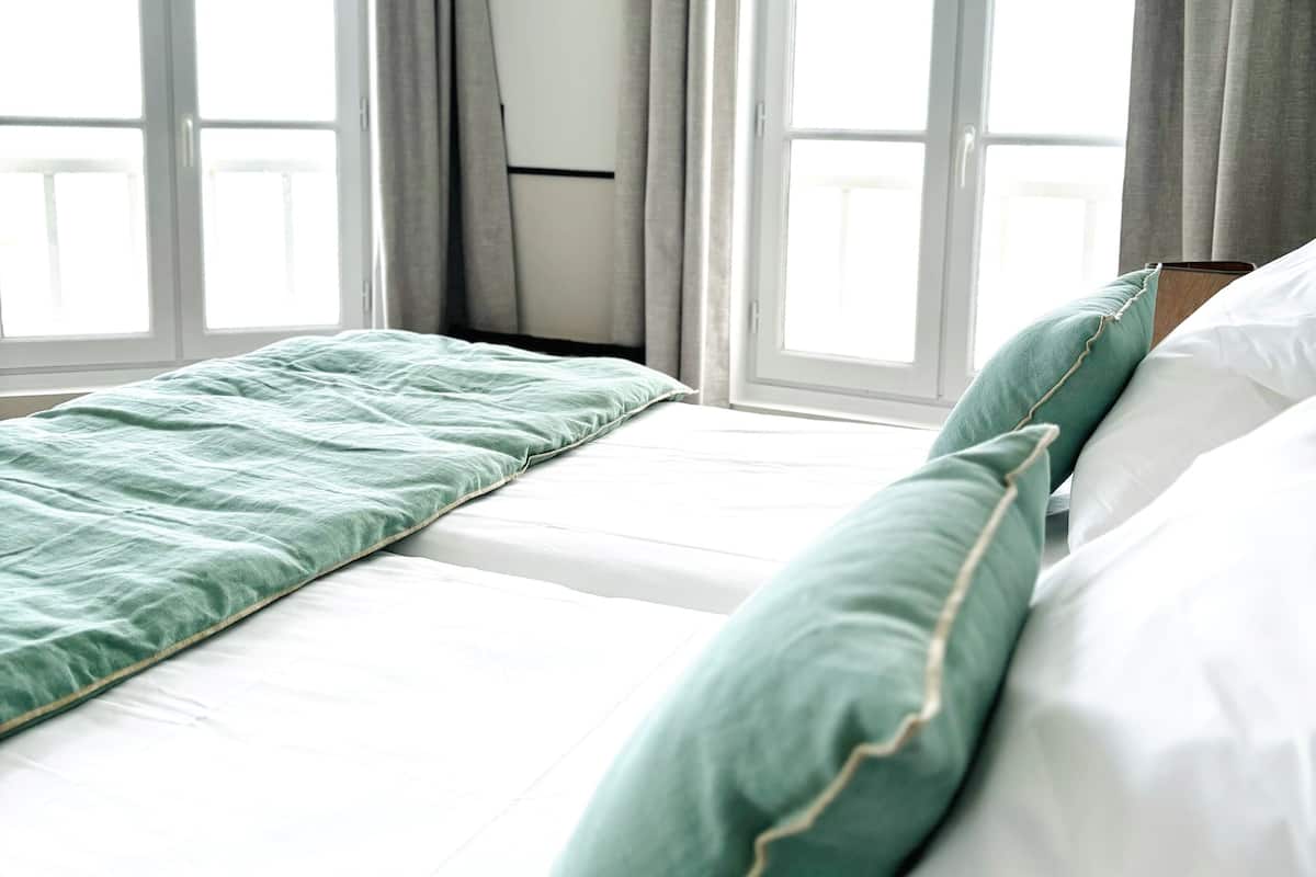 Une chambre d’hôtel avec deux lits, des rideaux gris et de grandes fenêtres.