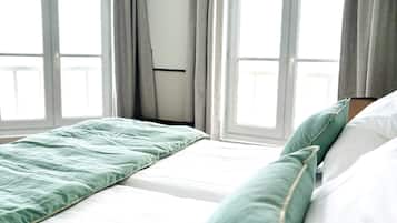 Une chambre d’hôtel avec deux lits, des rideaux gris et de grandes fenêtres.