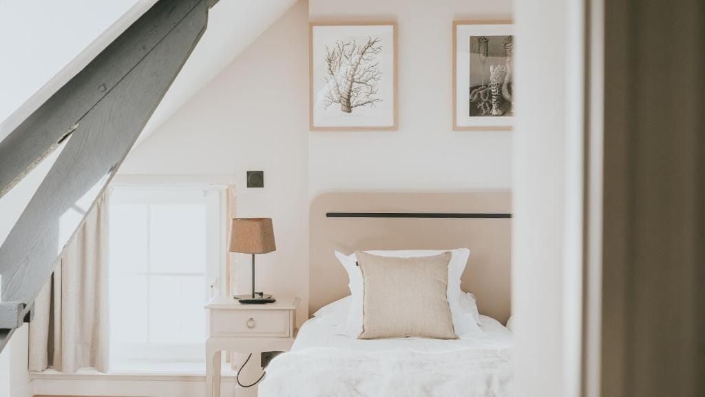 Un dormitorio con cama, mesita de noche, lámpara y cuadros en la pared.