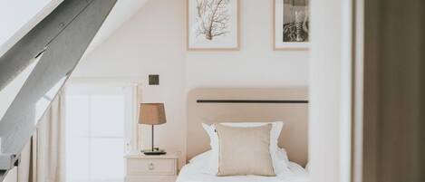 Un dormitorio con cama, mesita de noche, lámpara y cuadros en la pared.