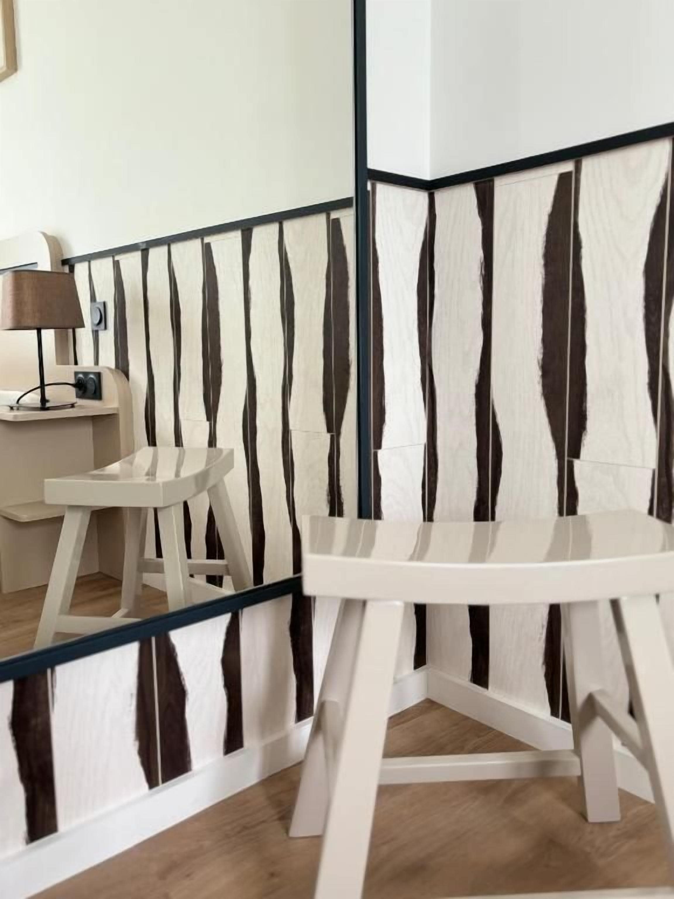 A corner of a room with a white and black striped wall, a white table, and a small white chair.
