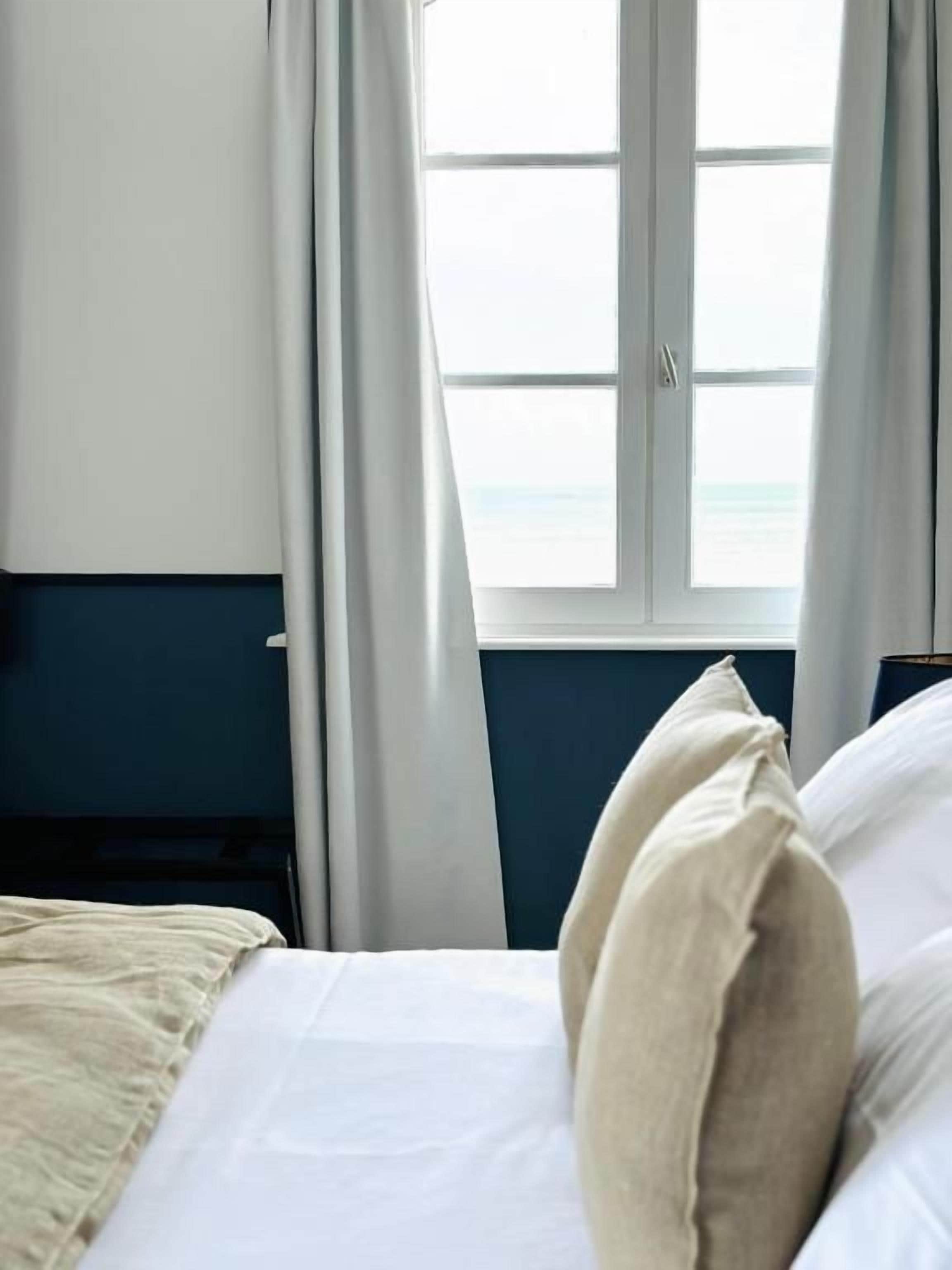 Una habitación de hotel con cama, ventana con cortinas y vista al mar.