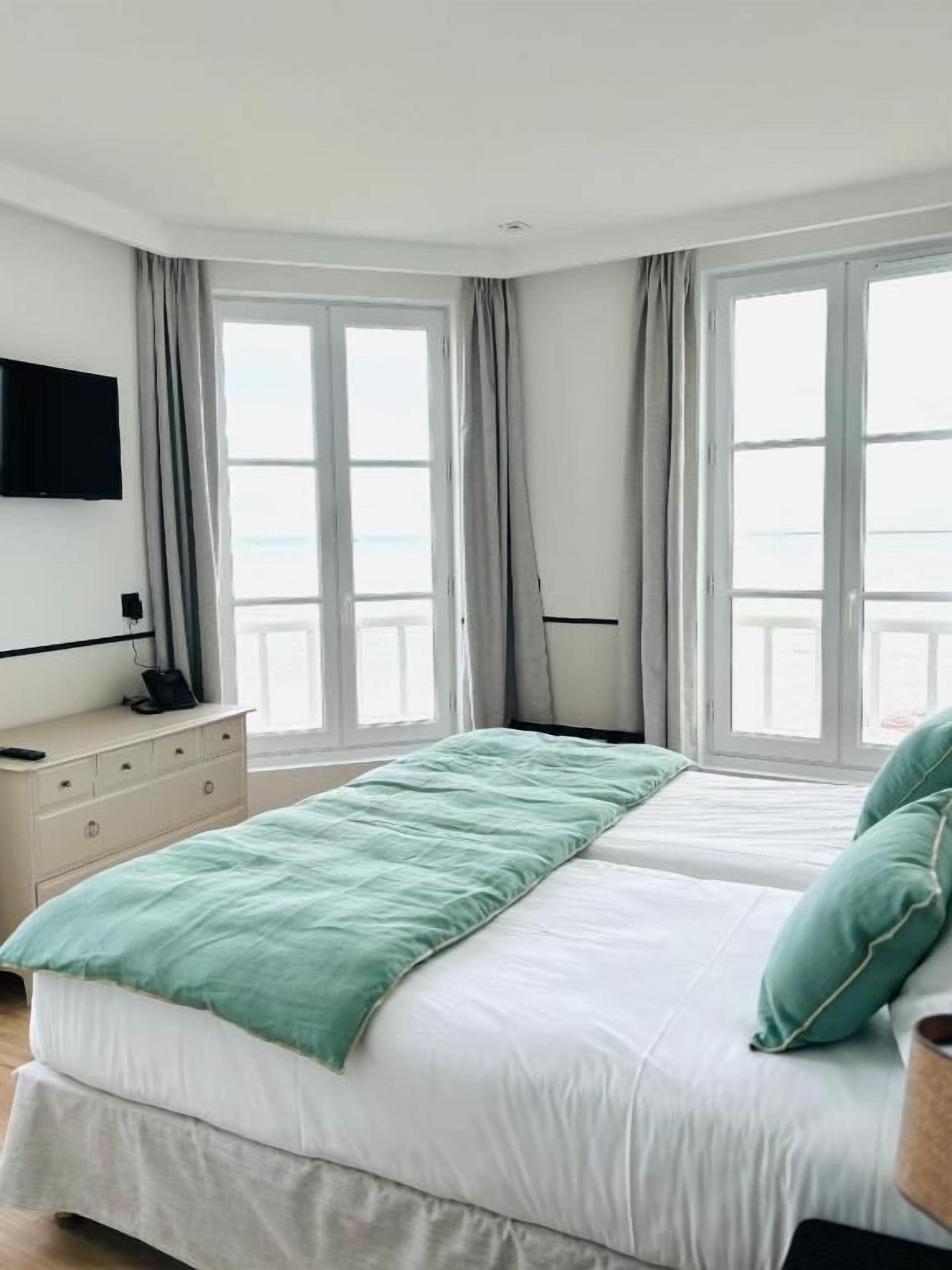 Un dormitorio con cama, cómoda, televisor de pantalla plana y ventanas grandes.