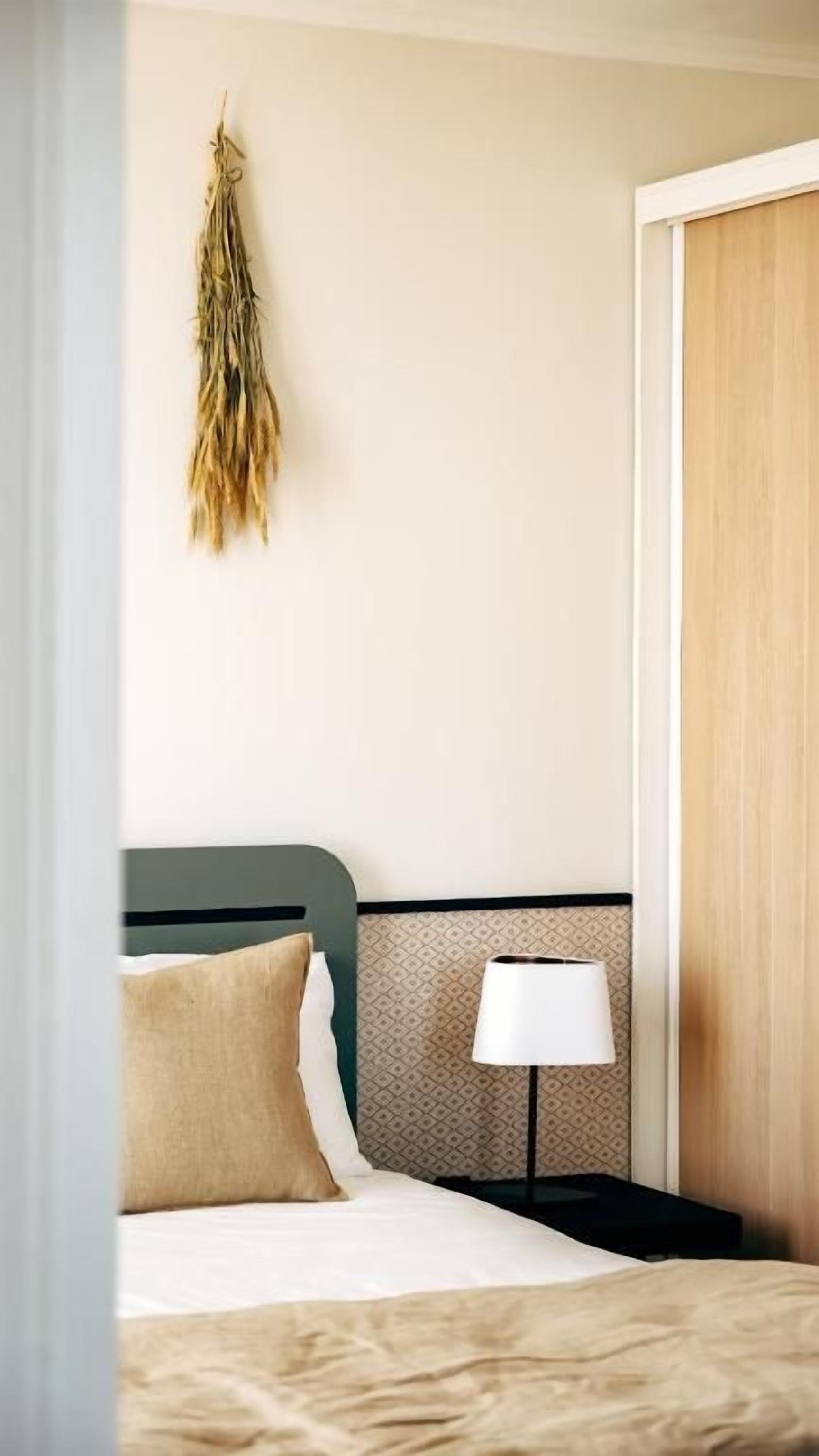 A neatly made bed with a headboard, a bedside lamp, and a hanging decoration on the wall.