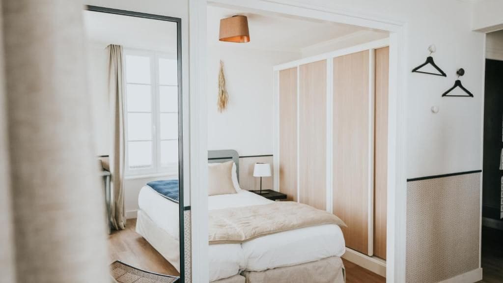 Una habitación de hotel con cama, mesita de noche, lámpara y un armario con espejo.