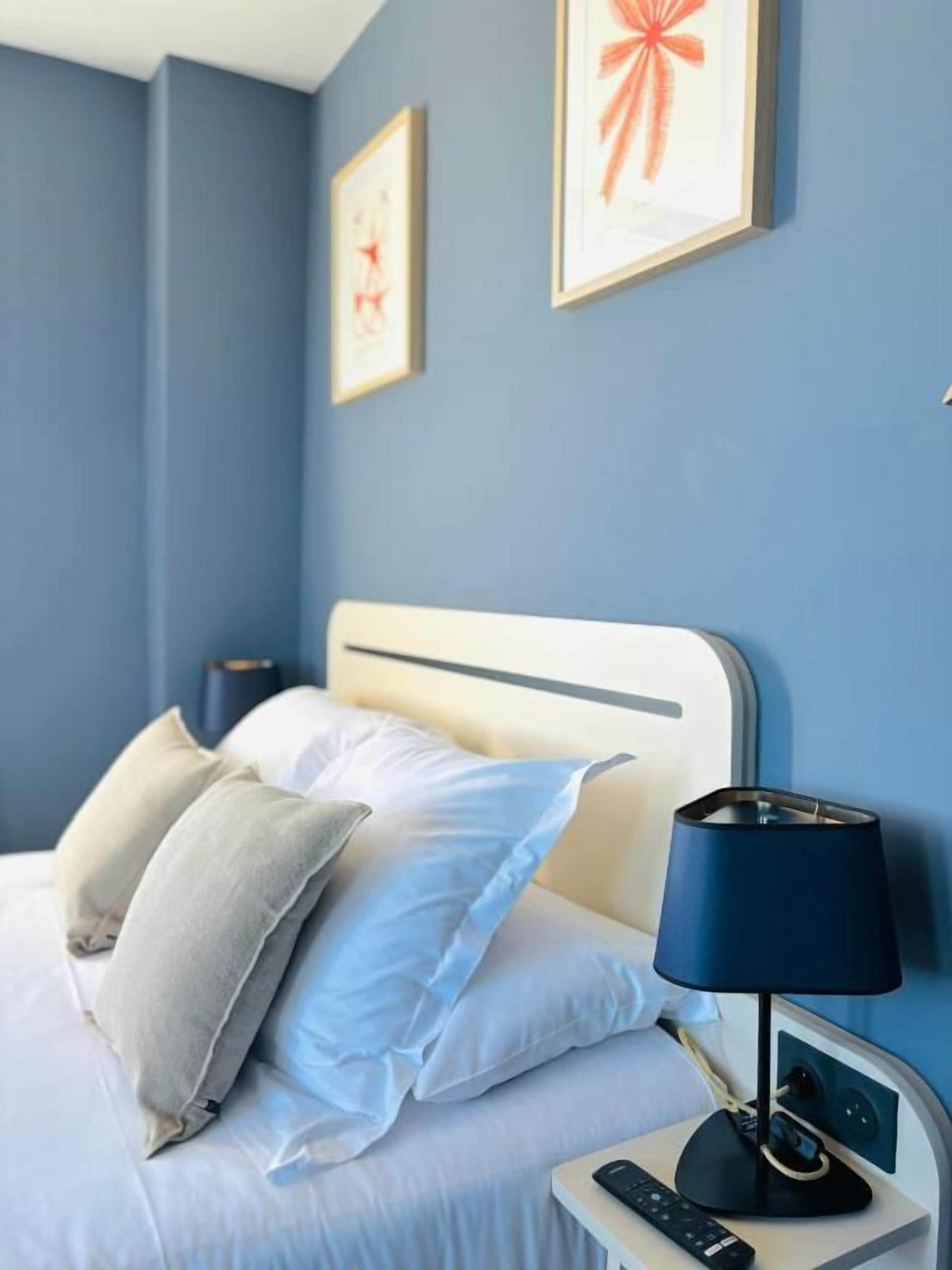 A hotel room with a bed, pillows, a bedside table with a lamp, and framed artwork on the wall.