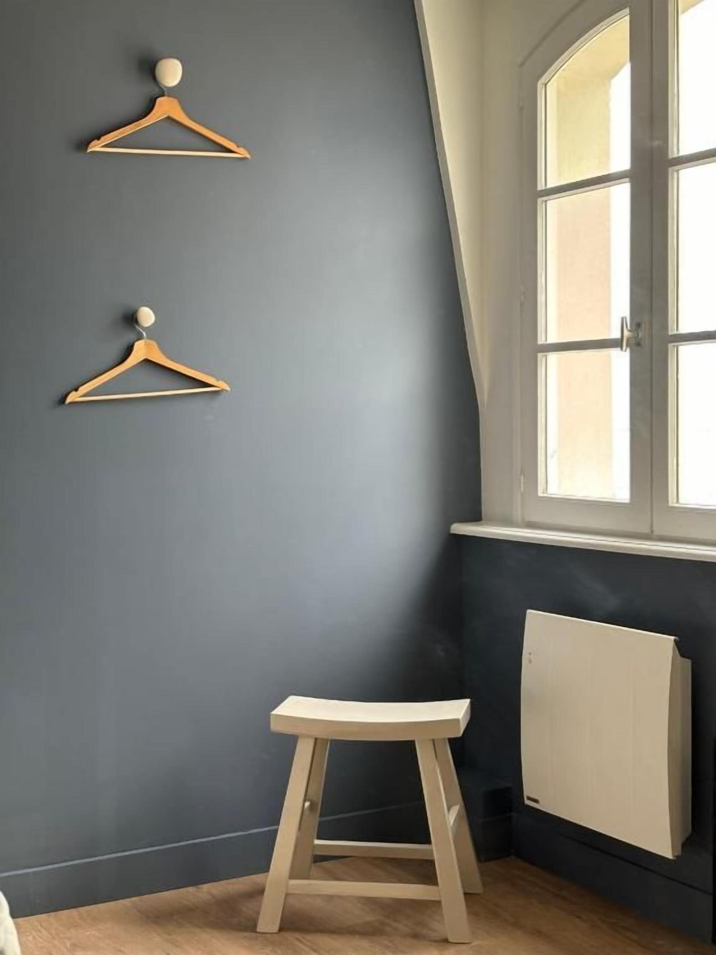 A corner room with a dark wall, a wooden stool, and two wooden hangers on the wall.
