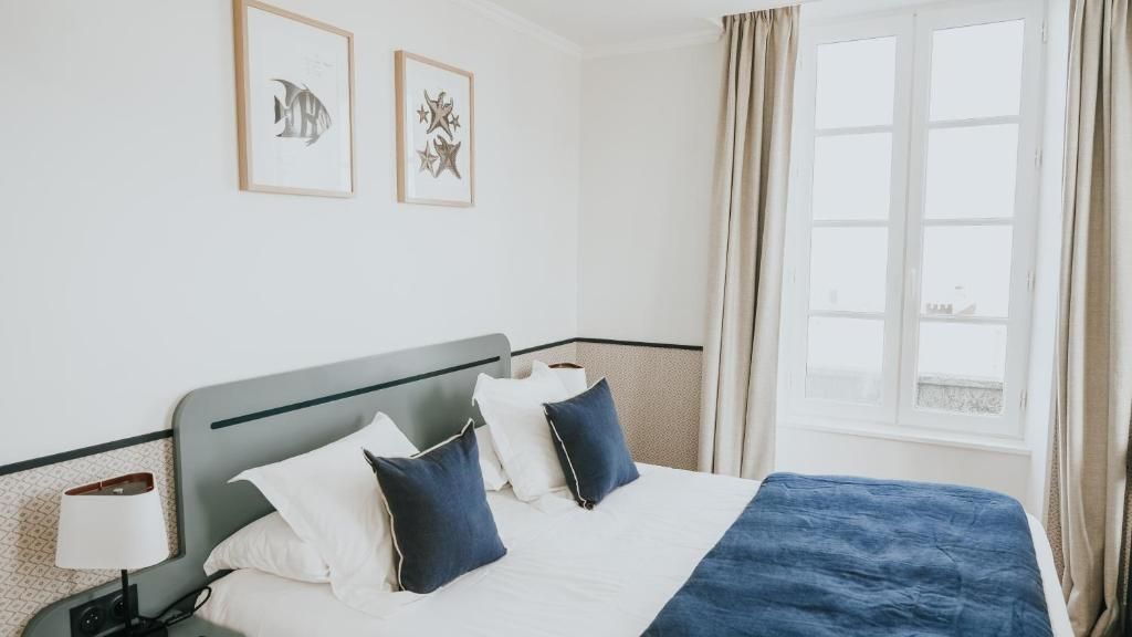 A hotel room with a bed, a nightstand, a lamp, and a window with curtains.