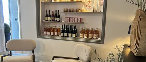 Una habitación con una estantería de pared para vinos que exhibe varias botellas, dos sillones tapizados, una cesta de mimbre con flores y una escultura de madera.