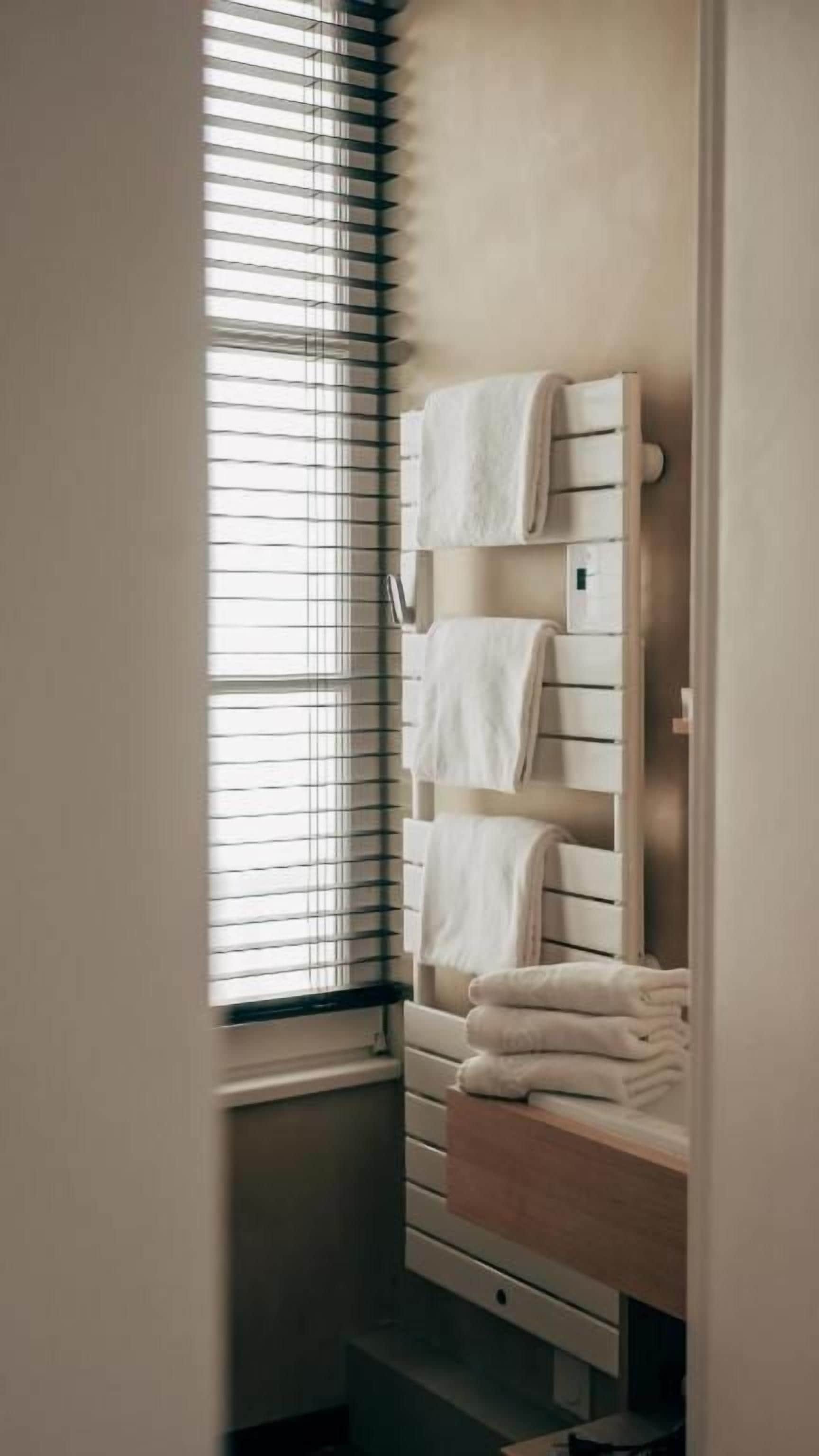 Une salle de bain équipée d’un porte-serviettes, d’une fenêtre avec des stores et d’un distributeur de serviettes.