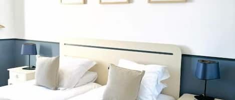 A hotel room with two beds, a nightstand with a lamp, and three framed artworks on the wall.