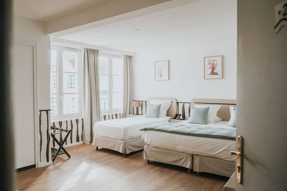 Une chambre avec deux lits, un plancher en bois et une fenêtre avec des rideaux.