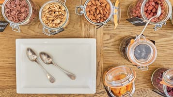 A wooden table with various food items in glass jars and a white plate with two spoons.