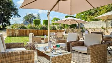 Un espacio de patio al aire libre con mobiliario de mimbre, incluyendo sofás y sillones, bajo grandes sombrillas.