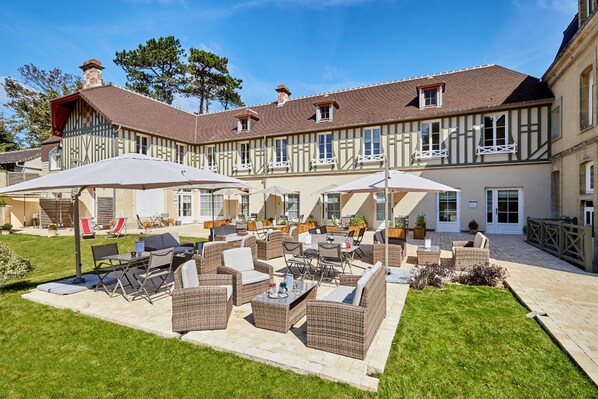 A courtyard with outdoor seating, a pool, and a building with a traditional facade. - Les Villas d'Arromanches (Tracy-sur-Mer)